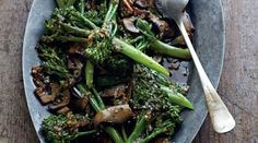 a plate filled with broccoli and mushrooms on top of a wooden table next to a spoon