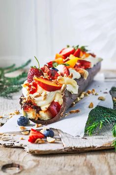 a dessert with fruit, nuts and other toppings on a cutting board next to some leaves