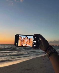 a person holding up a cell phone to take a photo on the beach at sunset