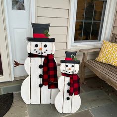 two snowmen made out of wood sitting on the front porch