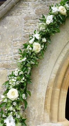 white flowers and greenery are arranged on the side of a stone church window sill