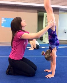 two girls doing handstands on the floor in an indoor gym with blue carpet