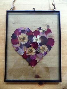 a heart made out of flowers hanging from a frame on a table with string attached to it