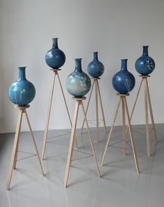 five blue vases sitting on top of wooden stands in front of a white wall