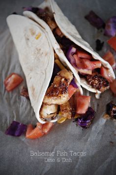 two tacos with meat, tomatoes and onions on a piece of waxed paper