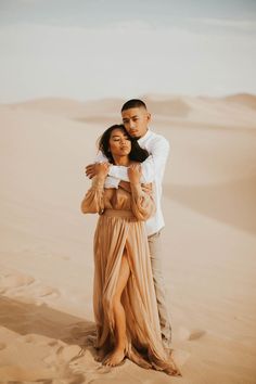 a man and woman hugging in the desert with sand dunes behind them for their engagement photos