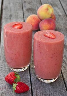 two glasses filled with fruit sitting on top of a wooden table next to peaches