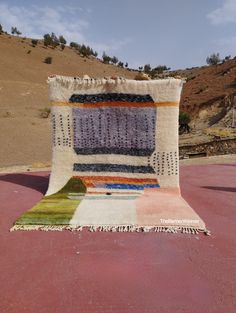 a multicolored rug on the ground in front of a hill with hills behind it