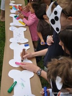 a group of children sitting at a long table with paper cutouts on it and crayons in front of them