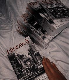 a person's hand on top of four books laying on a white bed sheet