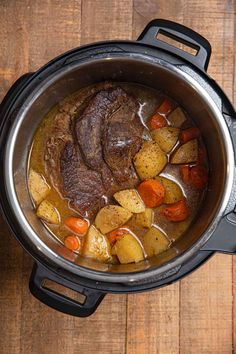 a pot filled with meat and vegetables on top of a wooden table