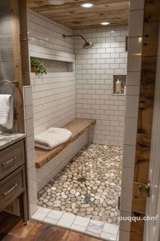 a walk in shower with rocks on the floor and wood ceilinging, along with white tile walls