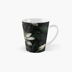 a tall mug with white flowers and green leaves on it, against a black background