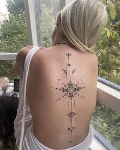 a woman with a tattoo on her back is sitting next to a dog and looking out the window