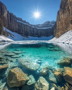 the sun shines brightly over an alpine lake surrounded by snow covered mountains and rocks