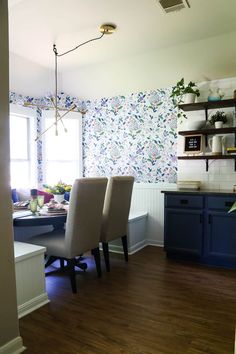 a dining room table and chairs in front of a wallpapered kitchen with blue cabinets