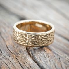 a gold wedding ring with an intricate design on the inside, sitting on a wooden surface