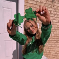 a girl in a green shirt is holding up some paper shamrocks on her head