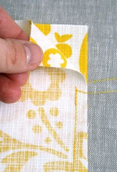 someone is stitching together fabric on the side of a piece of cloth with yellow and white designs