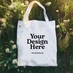 a white tote bag sitting in the grass with daisies around it that says your design here