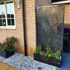 two black planters with flowers in them next to a brick wall and windows on the side of a house