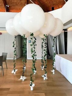 some white balloons and greenery are hanging from the ceiling in an indoor function hall