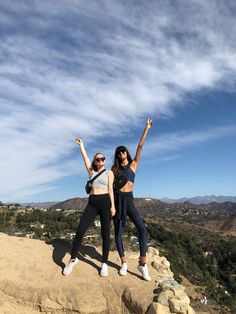 two young women standing on top of a mountain with their arms up in the air