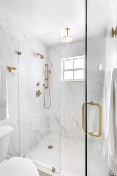 a white bathroom with gold fixtures and marble walls, along with a walk in shower