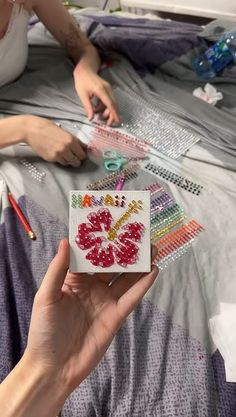 a woman is sitting on a bed with her hand holding a piece of beading