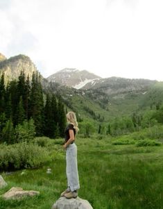 a woman standing on top of a rock next to a forest filled with green trees