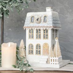 a small white house sitting on top of a table next to a candle