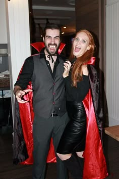 a man and woman dressed up in costumes posing for the camera with red capes over their shoulders