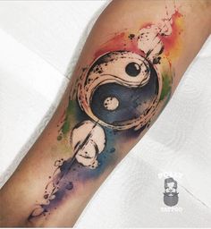 a watercolor tattoo on the arm of a person with a black and white yin symbol