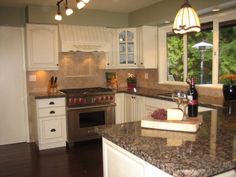 a kitchen with white cabinets and granite counter tops, an island in front of the stove