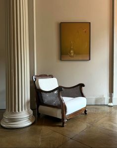 a white chair sitting next to a tall pillar in a room with columns on the wall