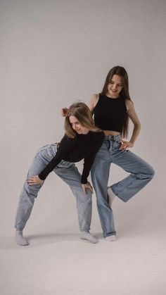 two young women are posing in jeans and crop tops with their arms around each other