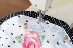 the sewing machine is working on the flowered tablecloth with polka dot trimming