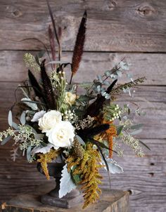 a vase filled with flowers and greenery on top of a wooden table next to a wall