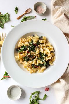 a white plate topped with pasta and spinach covered in sauce next to silverware