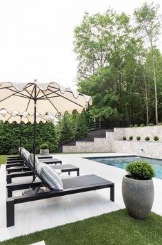 an outdoor patio with lounge chairs and umbrellas next to a swimming pool in the background