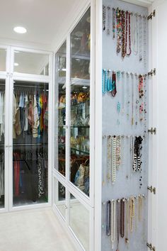 a closet filled with lots of necklaces and bracelets hanging on the wall next to glass doors