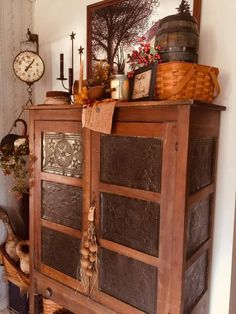 an old wooden cabinet with baskets and other items on it's top, next to a clock