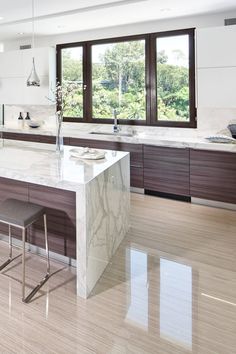 a large kitchen with marble counter tops and wooden cabinets, along with two bar stools