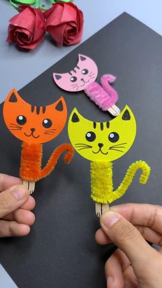 two handmade cats on toothpicks with flowers in the background, one is orange and the other is pink