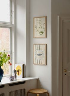 a room with some pictures on the wall next to a window and a stool in front of it