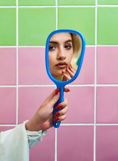 a woman holding a blue mirror in front of her face and looking into the mirror