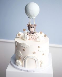 a white cake topped with a teddy bear on top of a cloud covered sky and stars