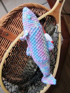 a crocheted stuffed fish sitting on top of a basket next to a wooden paddle