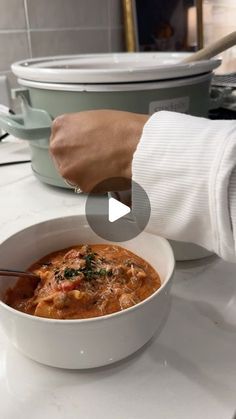 a person holding a spoon in a bowl of food on a counter top next to a casserole dish