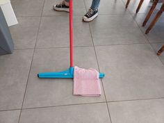 a person standing next to a pink and blue mop on top of a tile floor